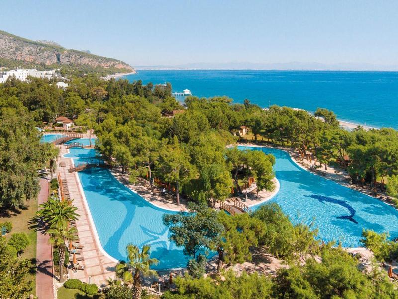 Resort with large pools surrounded by trees near a coastline and mountain.