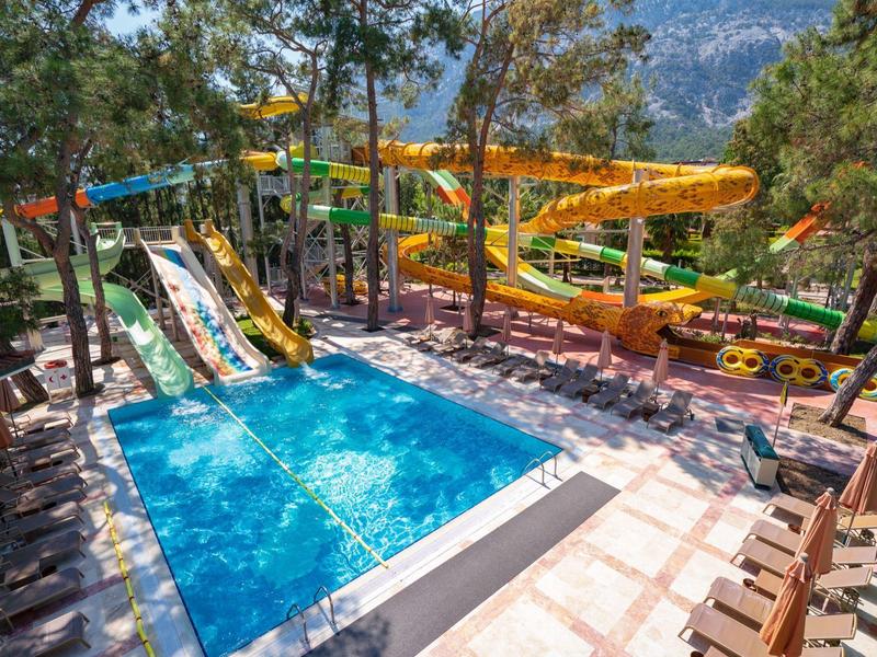 Outdoor swimming pool with water slides surrounded by trees and lounge chairs.