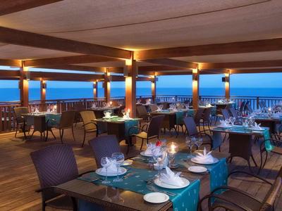 Restaurant en plein air avec vue sur la mer au crépuscule, tables dressées pour dîner.