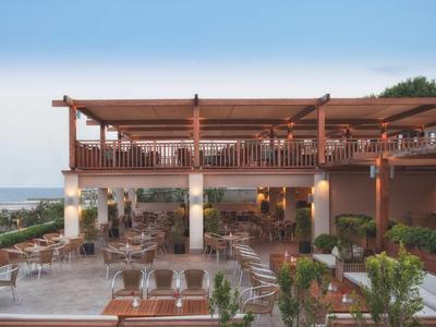 Terrasse d'hôtel avec tables, chaises en bois et vue sur la mer au crépuscule.
