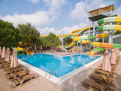 Belebter Hotelpool mit Wasserrutschen, Liegestühlen und Sonnenschirmen an einem sonnigen Tag.