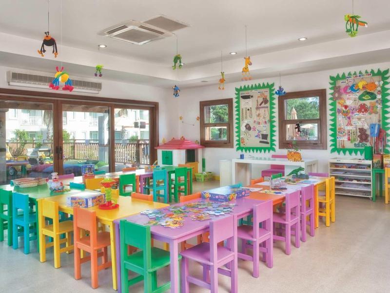 Salle colorée pour enfants avec tables et chaises multicolores, décor vibrant.