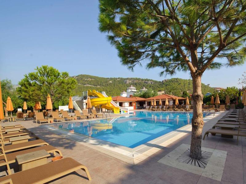 Piscine extérieure avec chaises longues et parasols dans un cadre verdoyant et ensoleillé.
