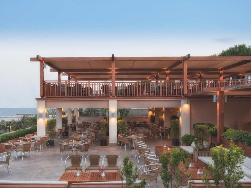 Terrasse d'hôtel avec tables, chaises en bois et vue sur la mer au crépuscule.