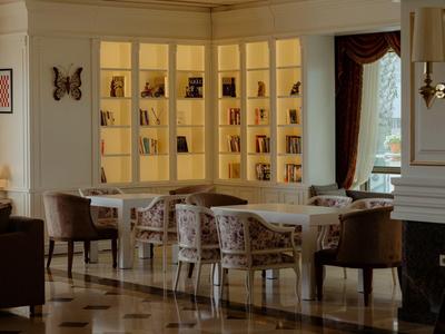 Elegancki salon hotelowy z krzesłami wokół stołu i oświetloną półką na książki.