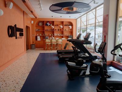 Moderner Fitnessraum mit Laufbändern, Peloton-Fahrrad und Regalen an orangefarbener Wand