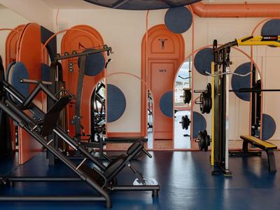 Moderner Fitnessraum mit Trainingsgeräten, Spiegeln und orangen Wandelementen.