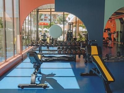 Moderner Fitnessraum mit Hanteln und Bänken, großen Fenstern und Blick ins Freie.