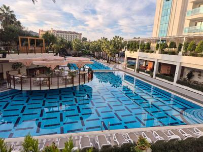 Großer Hotelpool mit blauen Kacheln, umgeben von Sonnenschirmen und Palmen.