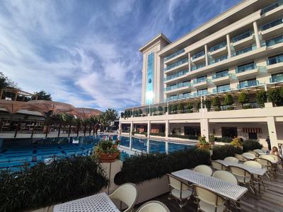 Nowoczesny hotel z odkrytym basenem, białymi leżakami i niebieskim, zachmurzonym niebem.