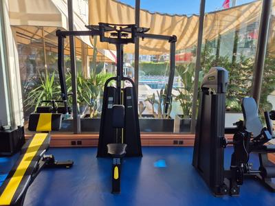 Innenraum eines Fitnessstudios mit verschiedenen Trainingsgeräten und großen Fenstern mit Blick nach draußen.