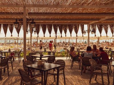 Zadaszony taras kawiarni z drewnianymi stołami i widokiem na zatłoczoną plażę.