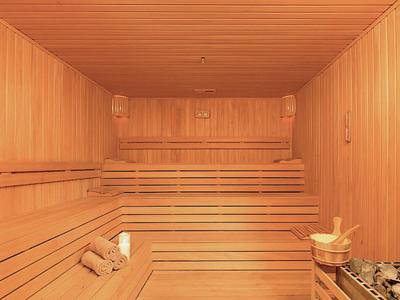 Przestronna sauna z jasnego drewna z kilkupoziomowymi ławkami i przytłumionym światłem.