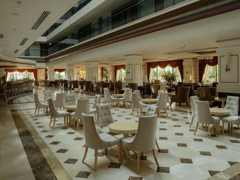 Przestronna, elegancka restauracja hotelowa z białymi krzesłami i okrągłymi stołami na kafelkowej podłodze.