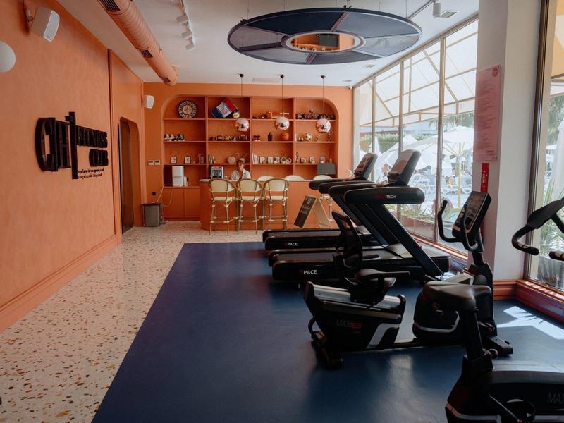 Siłownia z pomarańczową bieżnią i dużymi jasnymi oknami.