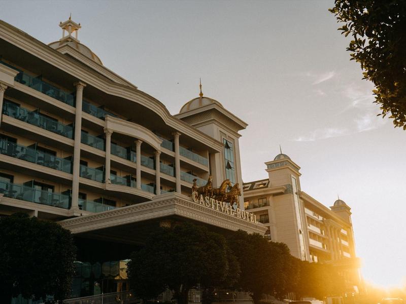 Budynek hotelowy z balkonami o zachodzie słońca, drzewa na pierwszym planie.