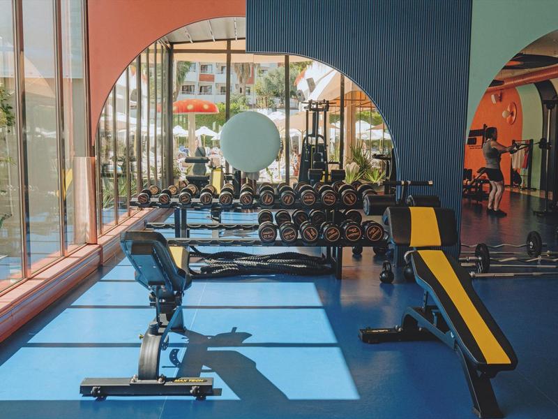 Jasna siłownia z nowoczesnym sprzętem i dużymi, łukowatymi oknami.