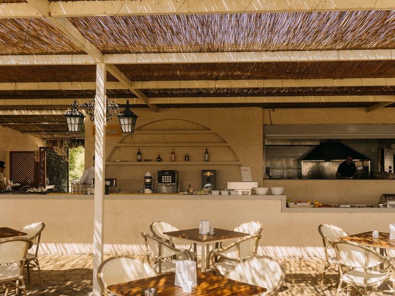 Kawiarnia na świeżym powietrzu z okrągłymi metalowymi stolikami pod drewnianym dachem.