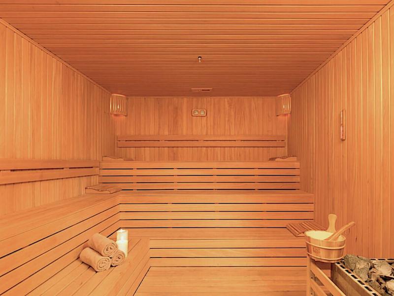 Przestronna sauna z jasnego drewna z kilkupoziomowymi ławkami i przytłumionym światłem.
