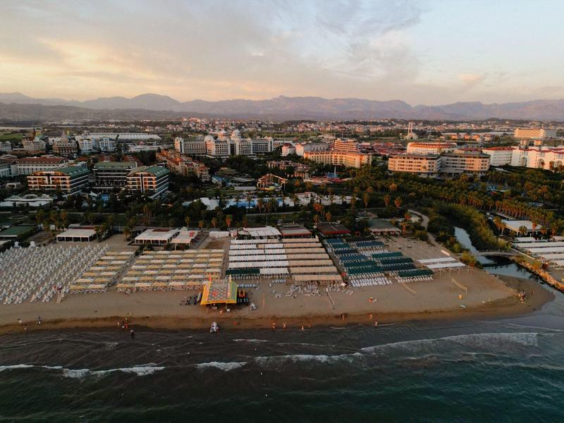 Plaża nad morzem z hotelami i górami w tle o zachodzie słońca.