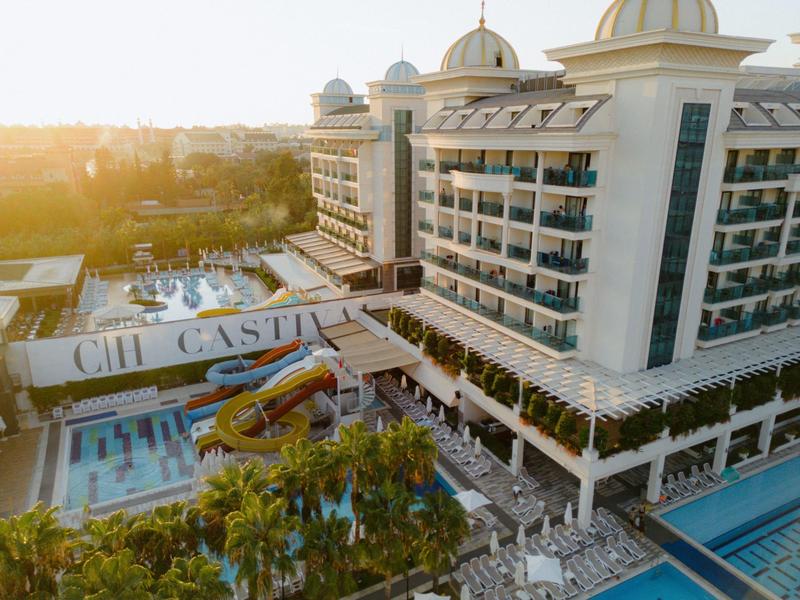 Widok na hotel z basenami, zjeżdżalniami wodnymi i palmami o zachodzie słońca.