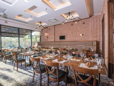 Restaurant d'hôtel moderne avec tables en bois, chaises en cuir et grandes fenêtres donnant sur l'extérieur.