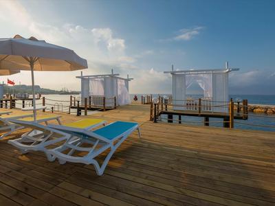 Strandlounge mit Liegestühlen, Sonnenschirmen und überdachten Pavillons auf Holzsteg neben Meer.