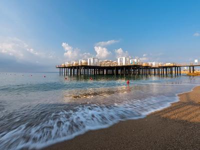 Spiaggia con onde delicate e molo in legno sotto cielo soleggiato con nuvole sparse