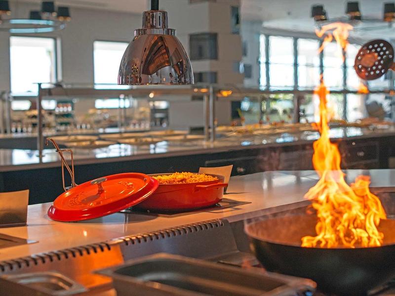 Cuisine ouverte avec poêle en flammes et ustensiles modernes dans un restaurant d'hôtel.