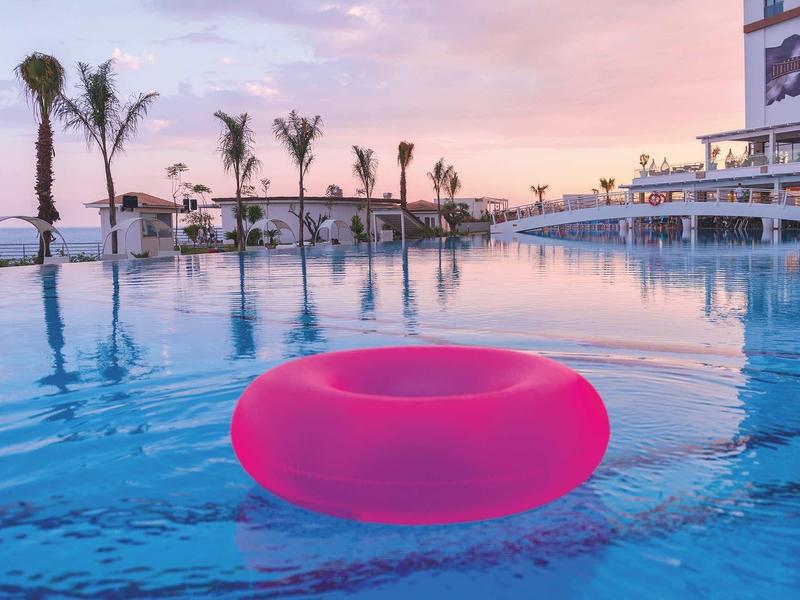 Bouée rose flotte dans la piscine de l'hôtel au coucher du soleil avec des palmiers en arrière-plan.