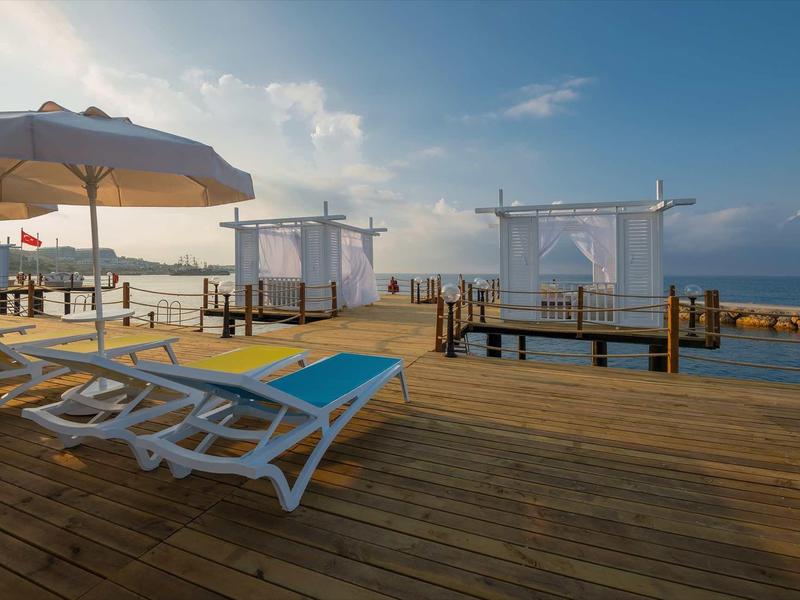 Lounge de plage avec transats, parasols et pavillons couverts sur une jetée en bois au bord de la mer.