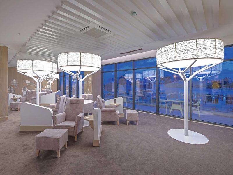 Chambre d'hôtel moderne avec grandes lampes sur pied design et sièges près de fenêtres du sol au plafond.