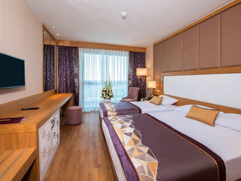 Chambre d'hôtel moderne avec lit double, télévision et coin salon près de la fenêtre.