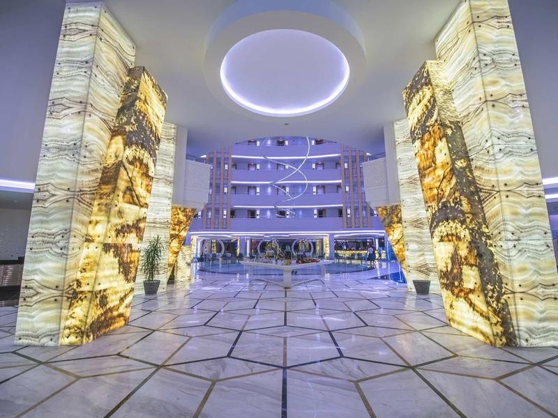 Grande entrée de hall d'hôtel moderne avec piliers en marbre éclairés et motif géométrique au sol.