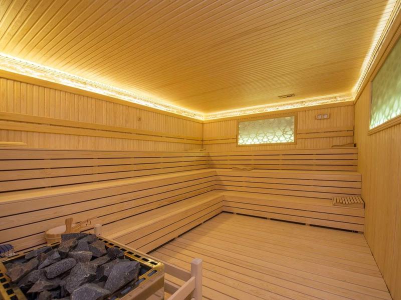 Sauna spacieuse avec revêtement en bois, longues banquettes et poêle à sauna avec pierres.