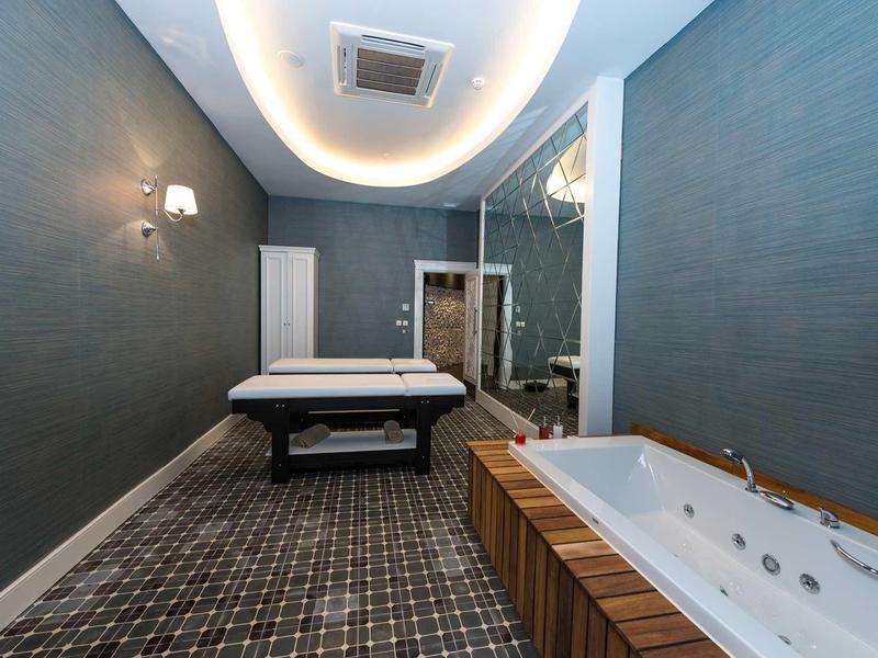 Salle de bien-être moderne avec table de massage, jacuzzi et éclairage tamisé.