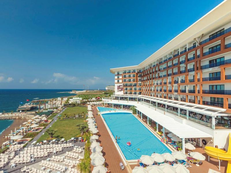 Complexe hôtelier moderne avec terrasse piscine et vue sur la mer sous un ciel bleu clair.