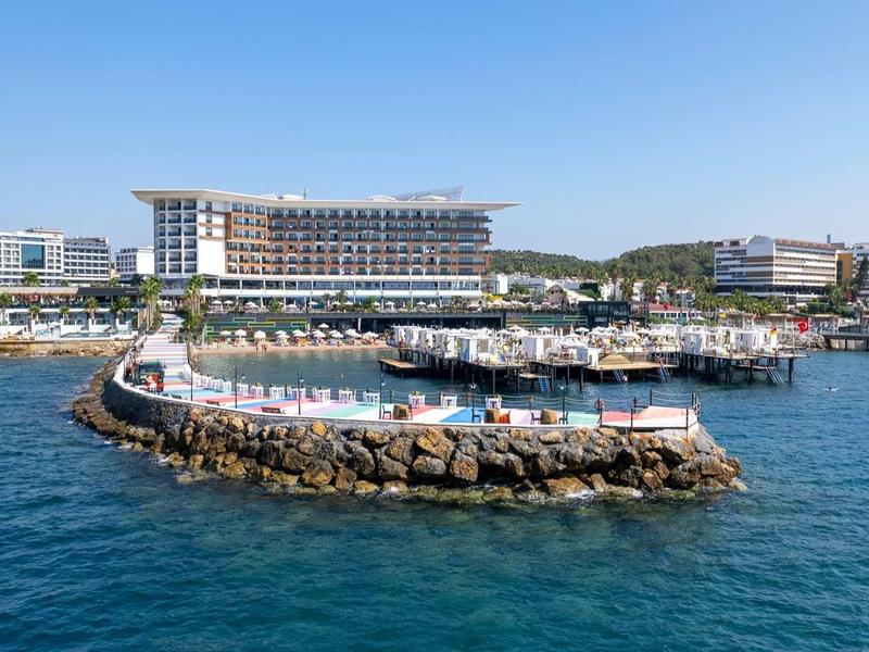 Petit complexe insulaire avec piscines et transats, entouré de la mer et d'hôtels en arrière-plan.