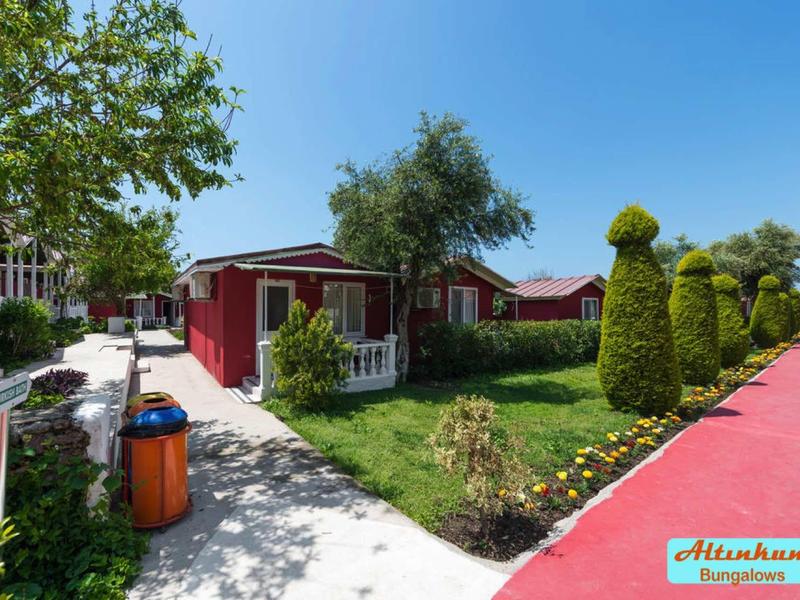 Sentiero rosso conduce a bungalow rossi con giardino curato e siepi verdi sotto un cielo blu.