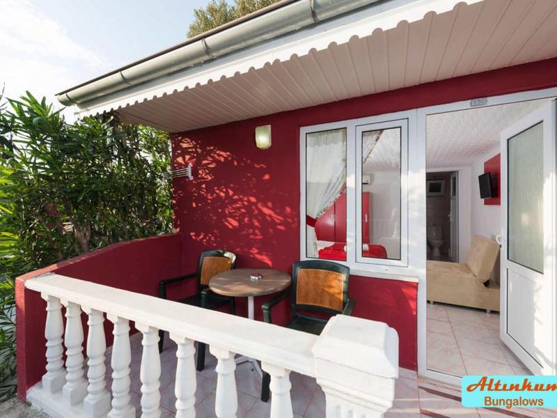 Balcone con ringhiera bianca su parete rossa, tavolo e sedie, con accesso a interno luminoso.