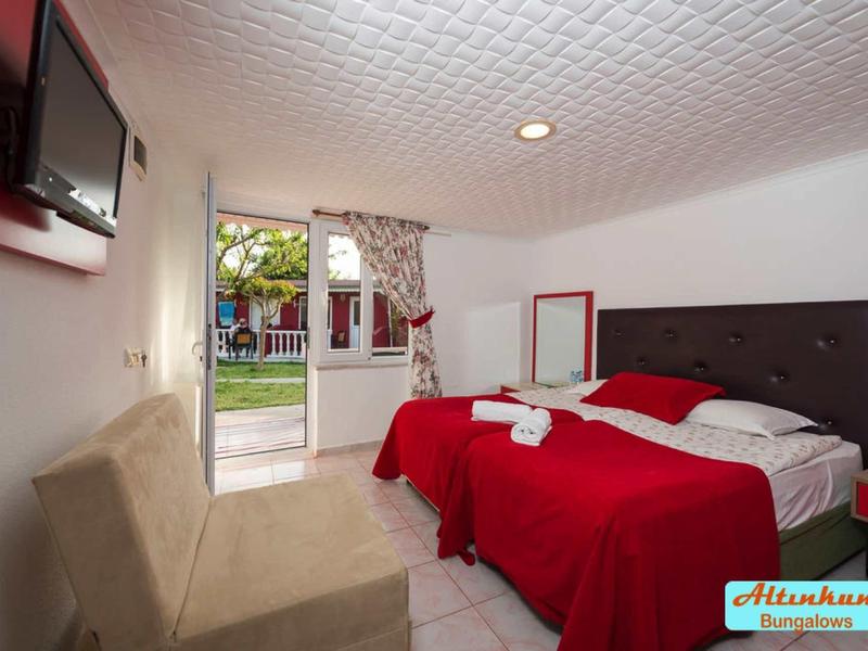 Camera d'hotel luminosa con copriletti rossi, TV e vista sul giardino attraverso la porta aperta.