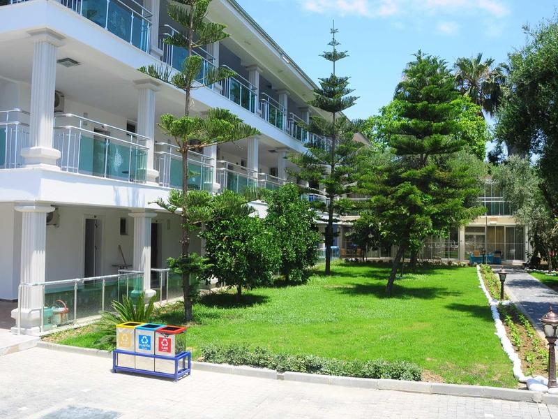 Moderní hotel se zeleným trávníkem, stromy a dětským hřištěm na dvoře.