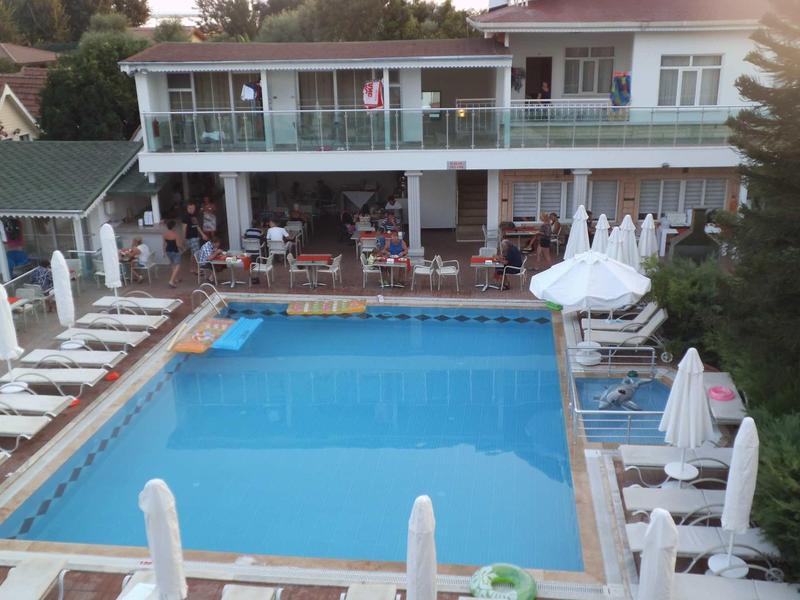 Velký obdélníkový bazén s bílými lehátky a slunečníky před dvoupatrovým hotelem.