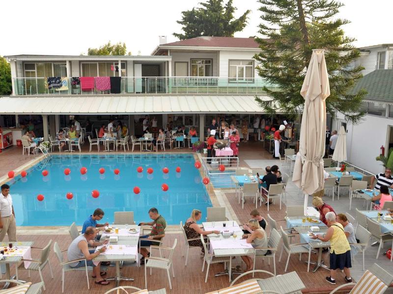 Hotelový bazén s posezením a hosty u venkovních stolů přes den.