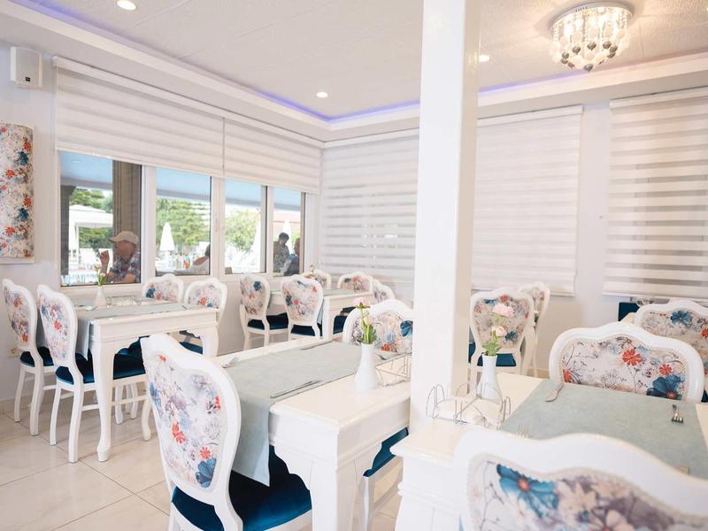 Světlá, elegantní jídelna s bílými stoly a židlemi s květinovým vzorem.