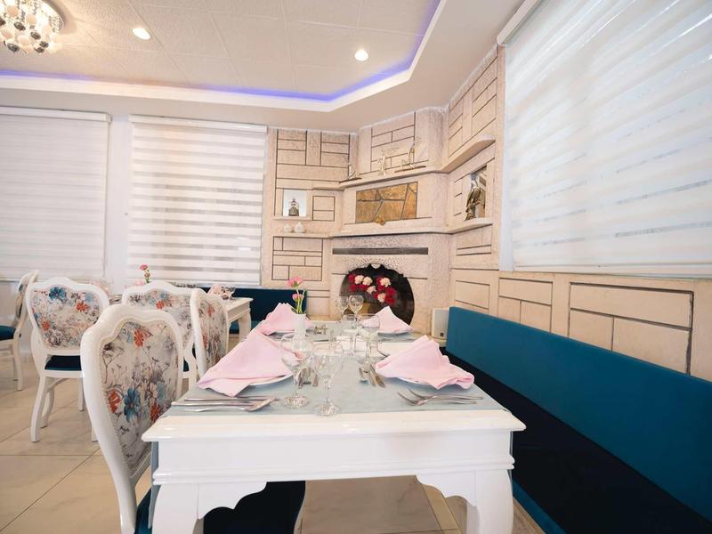 Elegantní interiér restaurace s bílými ubrusy a modrými lavicemi.