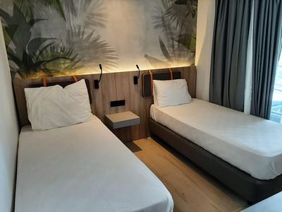 Habitación de hotel moderna con dos camas individuales, suelo de madera y grandes cortinas junto a la ventana.