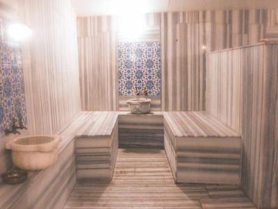 Baño turco moderno con paredes, bancos y lavabos de mármol bajo luz cálida.