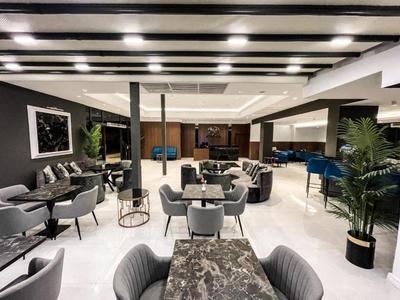 Interior moderno de lounge de hotel con sillas grises, mesas y techo de madera con iluminación LED.