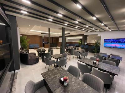 Salón moderno de hotel con muebles oscuros, mesas y iluminación acogedora.